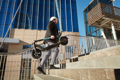 Man carrying GOTRAX Black GMAX Ultra High Performance Foldable Electric Scooter for Adults in Folded Position up stairs. 