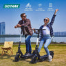 Two people riding Gotrax electric scooters with a cityscape in the background